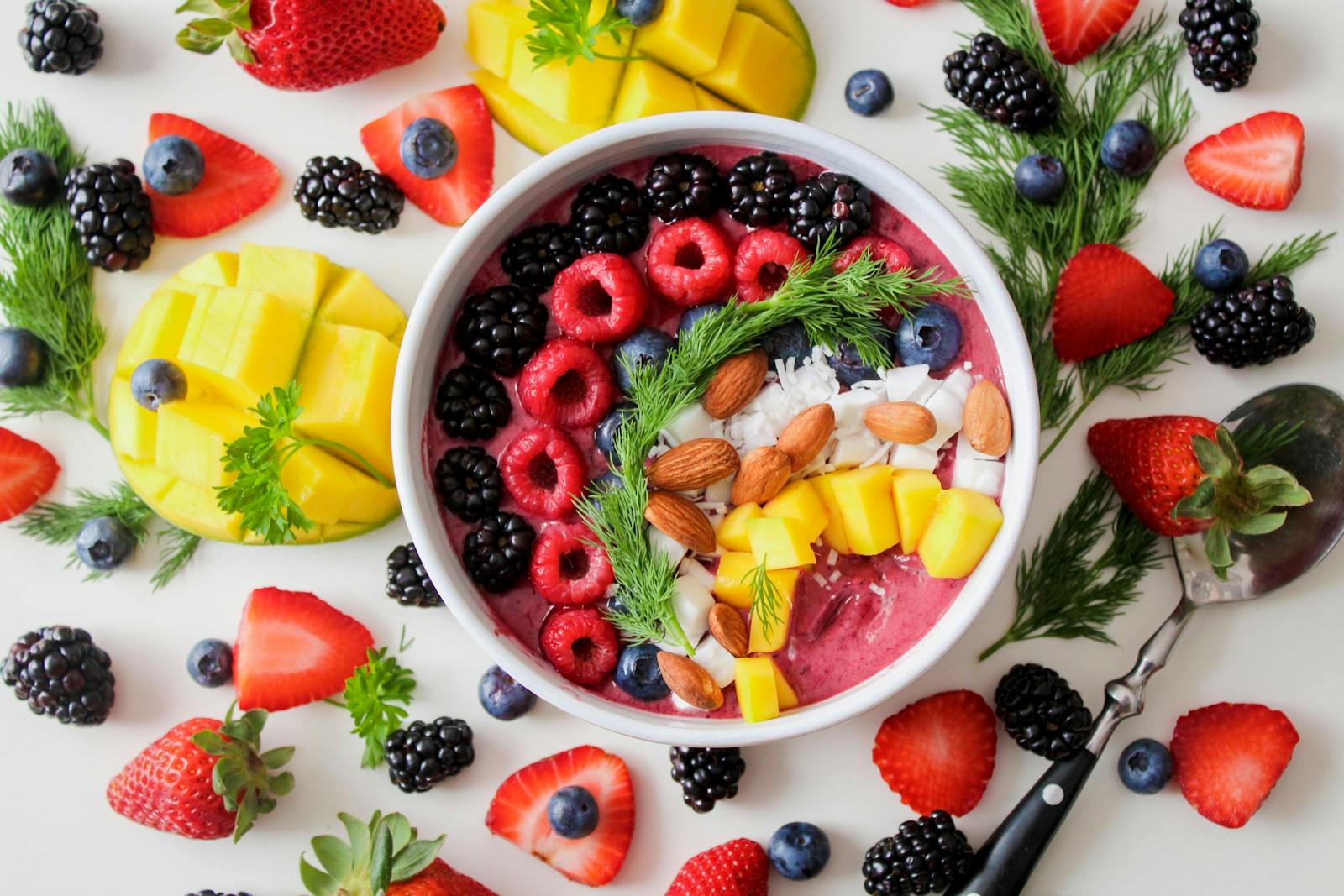 Overhead of a warm wooden breakfast table with a ceramic bowl of yogurt and berries, fresh ginger root, herbs, and a steaming mug of tea in morning light.